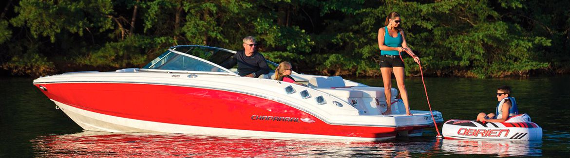 Three people sitting on a red boat that is tugging a child in a small raft